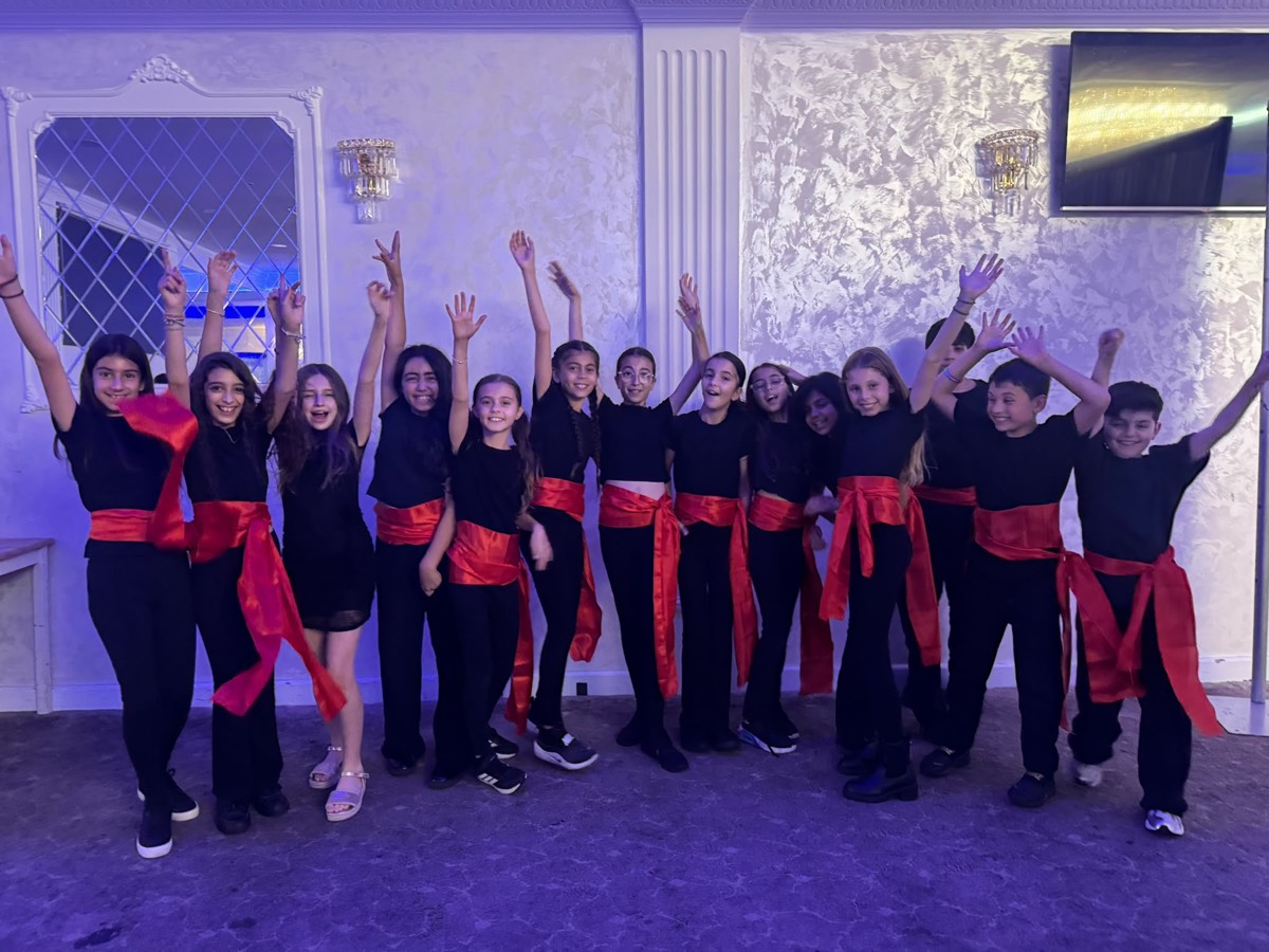 Our students in black with red sashes, arms raised after performing a Greek dance at the TGA Dinner & Dance